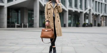 Woman wearing classic trench coat, structured handbag, and leather boots for a timeless 2025 investment wardrobe.