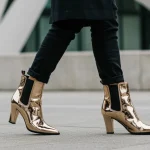 Stylish woman in metallic ankle boots walking in a modern city setting, showcasing fashion forward footwear.