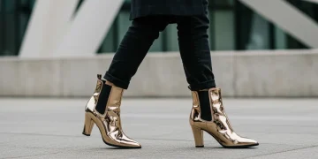 Stylish woman in metallic ankle boots walking in a modern city setting, showcasing fashion forward footwear.